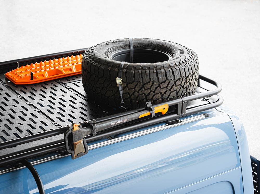 Spare tire secured to Sprinter camper van roof rack by cam straps with S-hooks