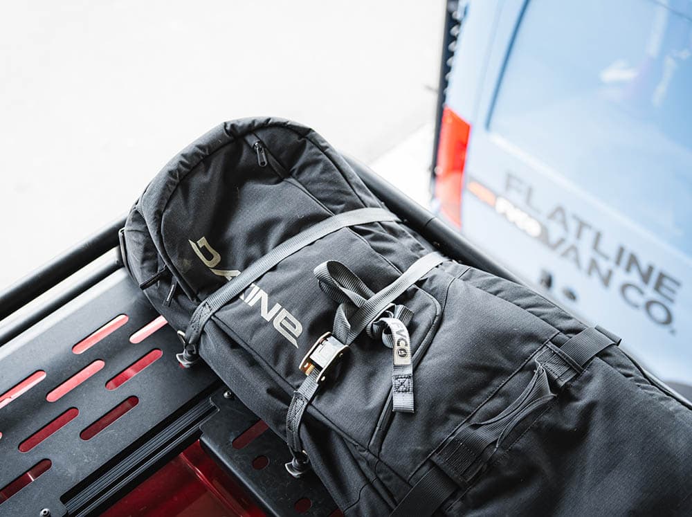 Snowboard bag secured to camper van roof rack with cam straps with L-track anchors