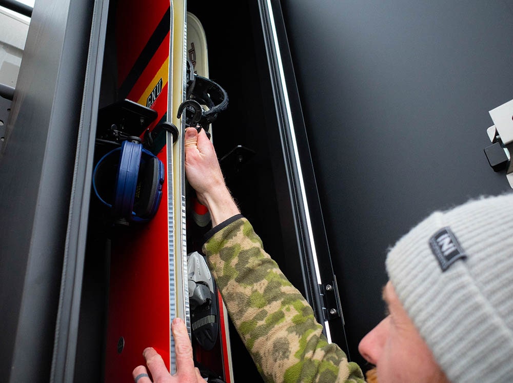 Loading up snowboards wit included hooks in the FVC Ski & Snowboard Locker for camper vans