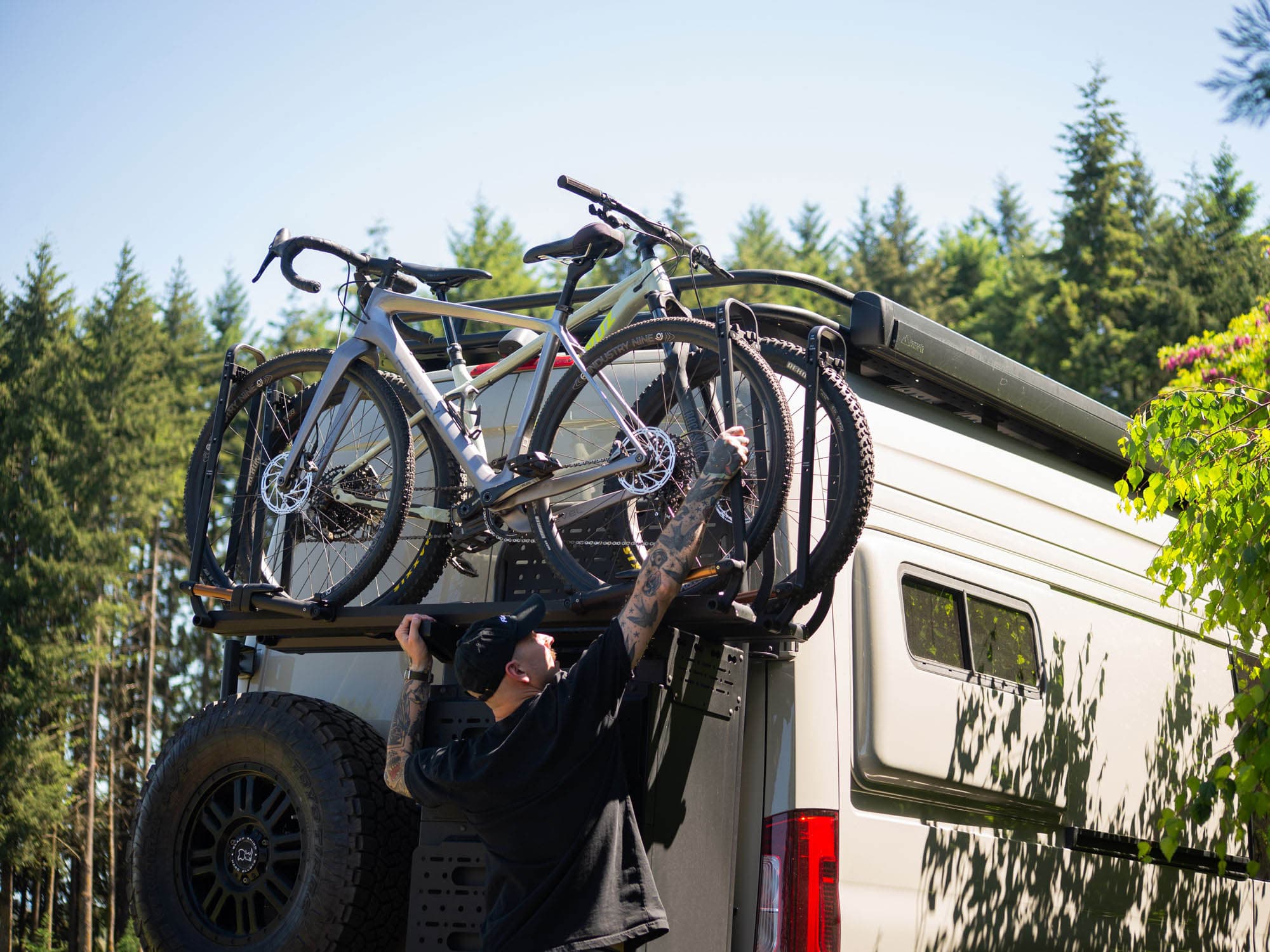 Person securing bikes onto Kuat bike rack trays mounted on Rear Storage Box Bike Rack Mount Adapter