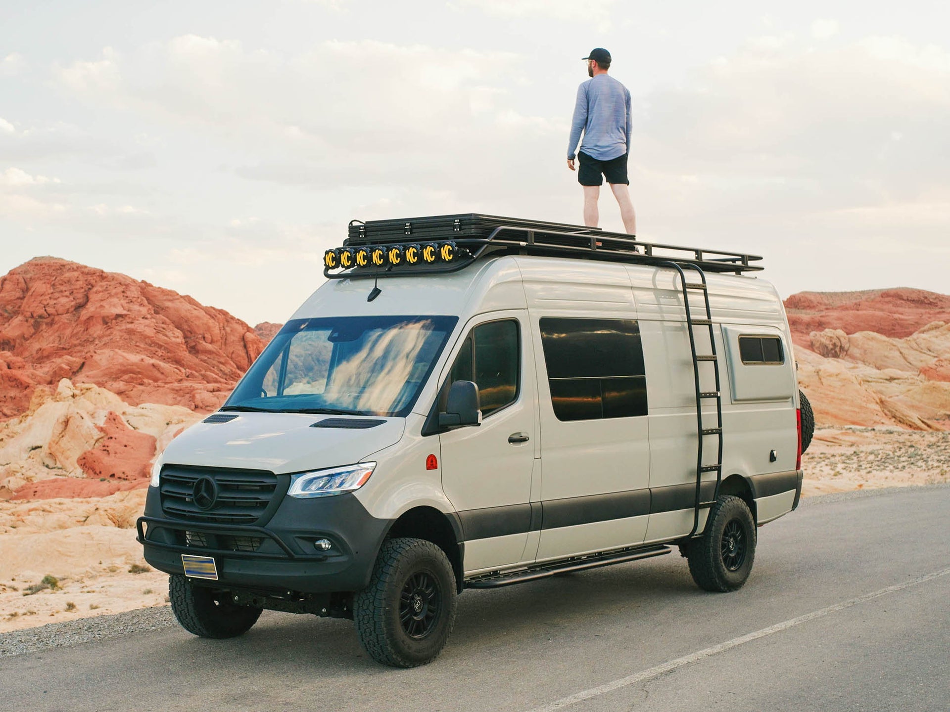 Sprinter Apex Side Ladder installed on 170 camper van with person standing on the Safari roof rack