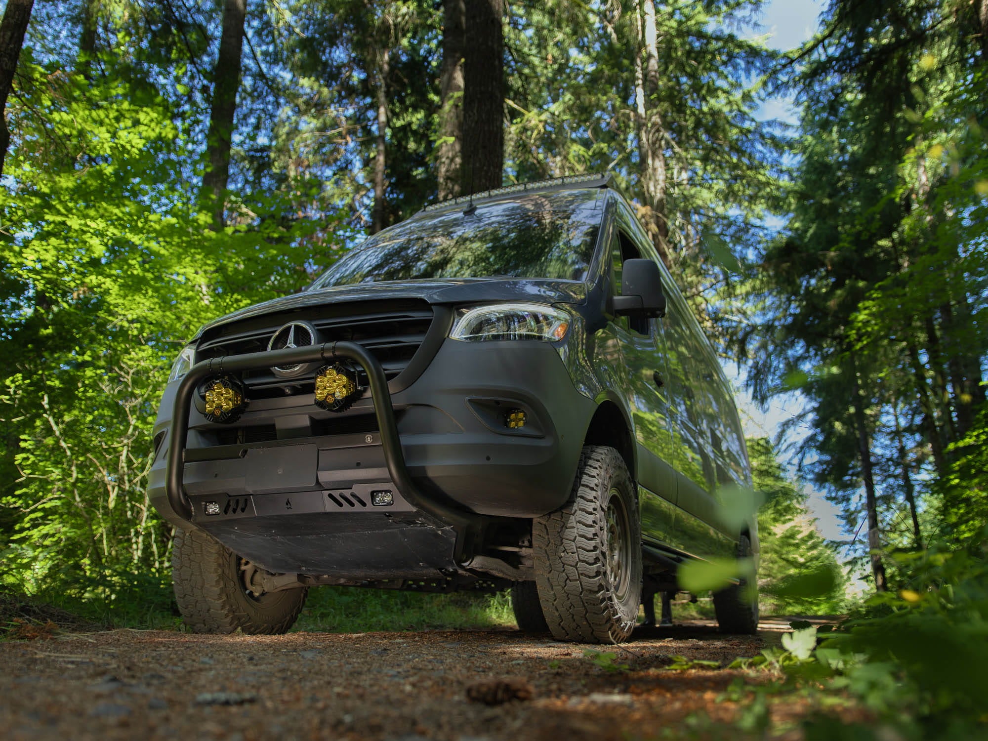 Low-angle view showing Sprinter Skid Plate installed with Sprinter Van Bull Bar on van parked in the woods